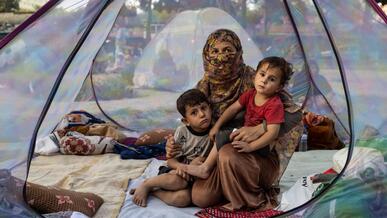 A recently widowed Afghan woman, 28, sits on the floor of a net tent holding holding her two children in a makeshift camp for displaced families in Afghanistan.