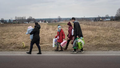 A family that fled the conflict in Ukraine walks along a rural Polish road in winter, carrying a baby and bags of clothes and supplies.