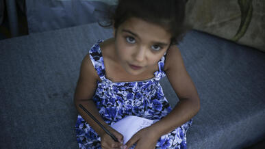 A young Syrian refugee girl writes in a notebook.