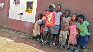 Children stand and pose for a picture in front of a red wall built by the IRC.