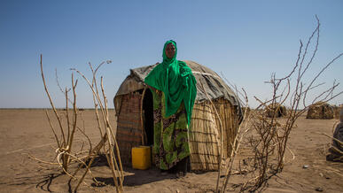Woman stands in front of temporary shelter in drought-afflicted region.
