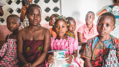 Women and children dressed festively sit at an indoors gathering in Ivory Coast.