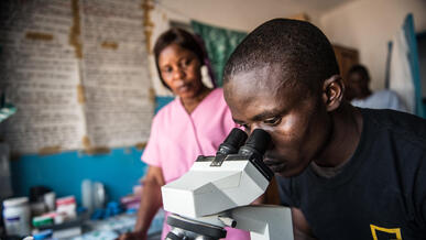 An IRC health worker testing for the Ebola virus examines a sample on slide on a microscope