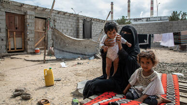 A mother and her two young children seated outdoors in Yemen