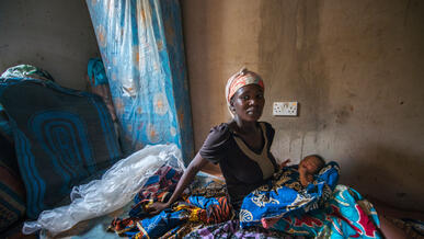 A Nigerian woman sits on a mattress with her infant child.