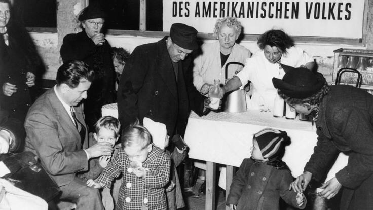 food distribution to families. In the background a poster saying "Spende des amerikanischen Volkes".