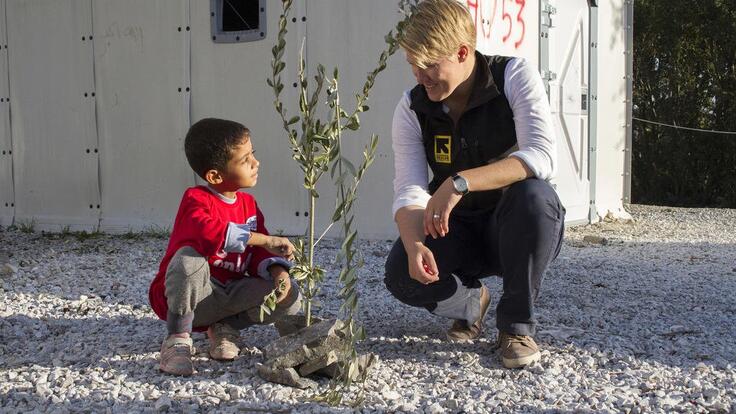 A young boy and IRC worker crouching besides a baby tree