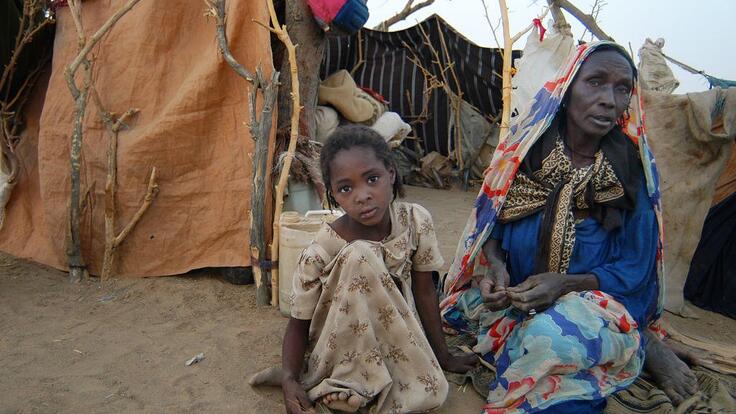 A young girl and a elderly woman in front of a poor tent