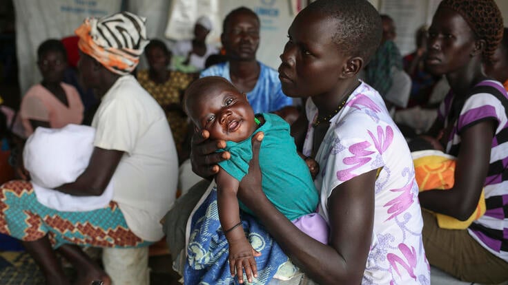 A baby smiles in their mother's arms. South Sudanese refugees wait to get their babies vaccinated, at the Koro Health c Bidi Bidi, Uganda.