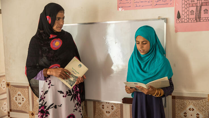 Bibi Asha reads from a book while her teacher looks on 