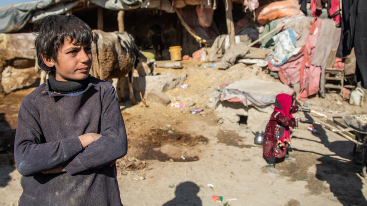 A boy, living in Ghaibi Bala camp in Kabul, Afghanistan, looks on as his mother is interviewed by International Rescue Committee (IRC) staff to see if she meets the criteria to receive a cash distribution from the IRC. The impact of Afghanistan's economic problems is evidenced by the conditions of his surroundings.