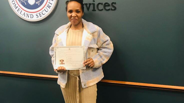 A woman standing with a certificate in front of a seal. 