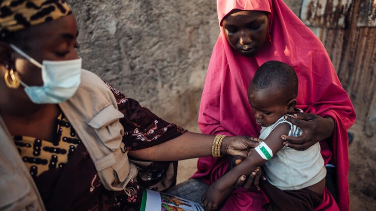 IRC Nutrition Officer Fatima Wakilamtu teaches Bilkisu Muhammad how to measure her child’s arm using a MURAC tape at her home in Maiduguri, Borno, Nigeria. 