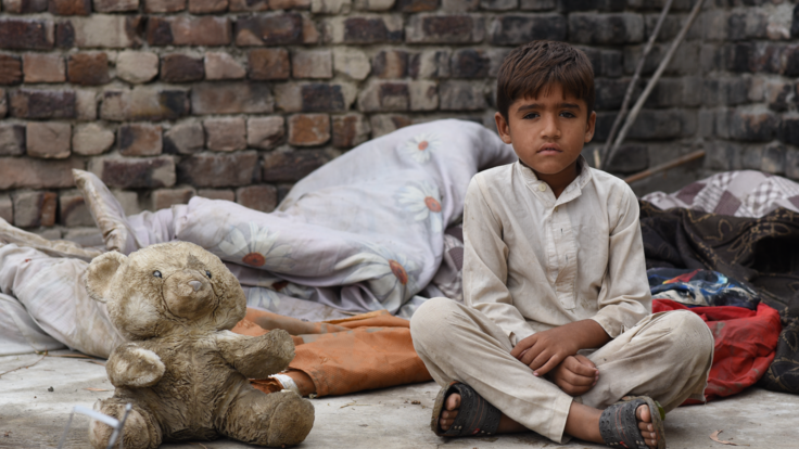 A boy sits with his legs crossed next to a dirty teddy bear.