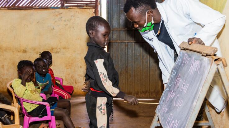 A child stands at the front of the class learning the alphabet.