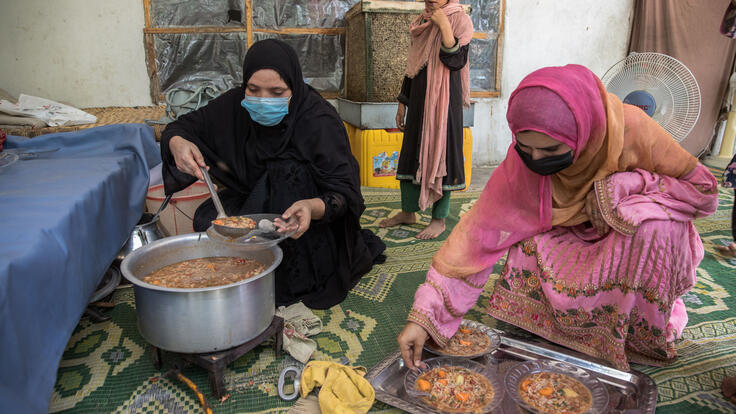 Barfi (i svart), en RESCUE-volontär, sitter på golvet och lagar mat. Hon får hjälp av Rahullah, en volontär.