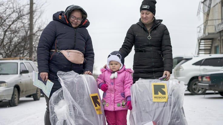 Eva stands between her old family members who hold packages marked with the IRC's logo.
