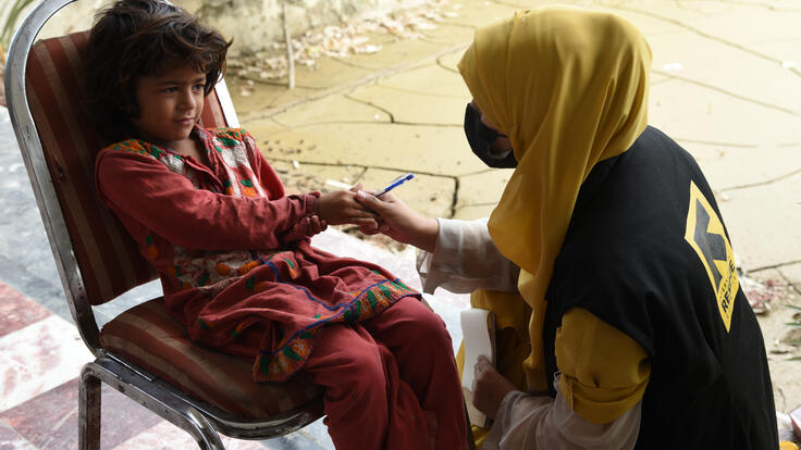 An IRC staff member shakes the hand of a young girl sitting in a chair.