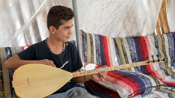 Yasser sits at sofa and plays his buzuq.