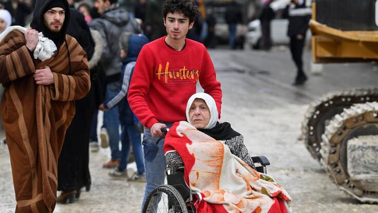 Jordbävning Turkiet Syrien: Två unga män hjälper till att evakuera en äldre kvinna i rullstol.