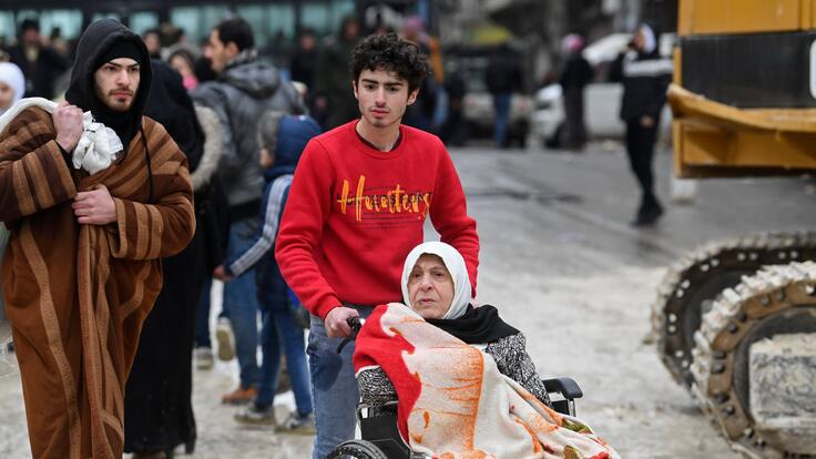 A young man pushes an woman in a wheelchair in the aftermath of an earthquake. Photo by AFP via Getty Images