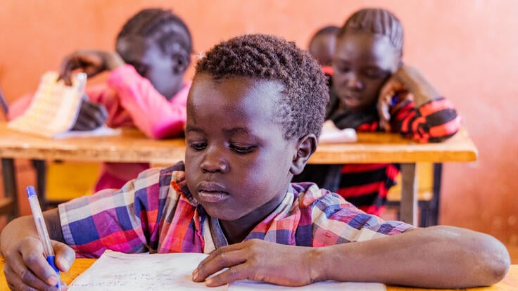 A young boy works on a writing exercise. Other students are doing the same behind him.