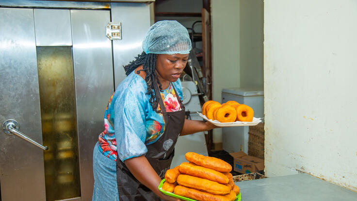 Harriet carries two plates full of pastries from a kitchen.