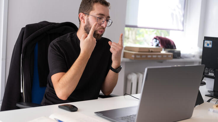 Oleksii sits at his desk and uses sign language on a video call to help deaf Ukrainian refugees as the resettle in Poland.