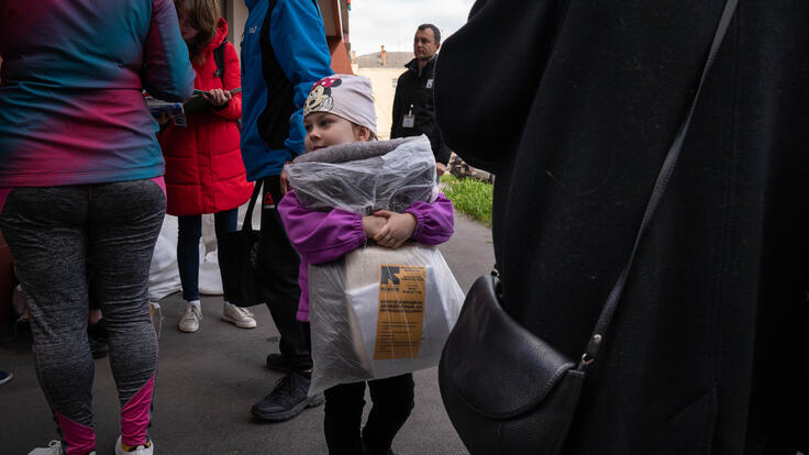 A young girl in the Dnipro region holds blankets she received from the IRC. The package of blankets and winter materials is almost as large as she is.