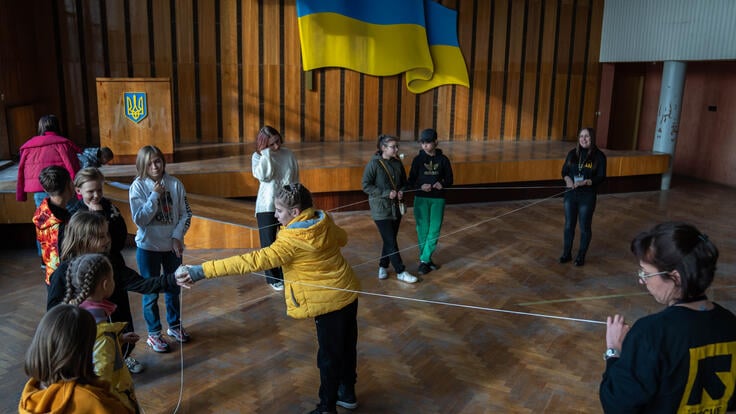 Children complete an activity together at an IRC-supported safe space. A Ukrainian flag hangs in the background.