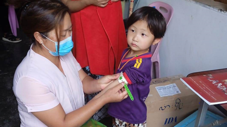 At the clinic of the internally displaced people camp, a health worker uses the mid-upper arm circumference measure (MUAC) to quickly identify if the child is at risk of malnutrition. When measured properly against a bare upper arm, the paper gauge provides a number and indicates the colour range. The green colour here is positive - the child is not showing signs of malnutrition.