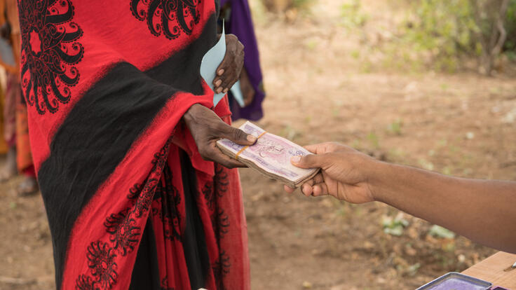 Two people exchange a stack of Ethiopian currency. The bills are pink in color.