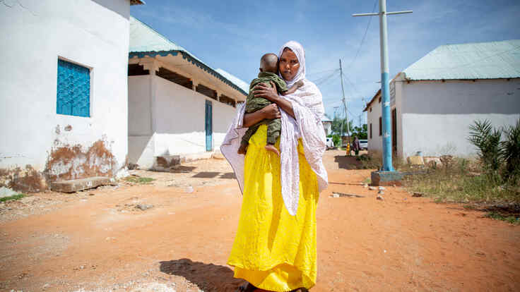 Fartun stands in the street, holding her baby son.