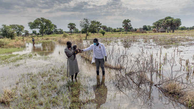 Abuk Deng holds her four year old daughter in her arms as they walk away from their flooded home while an IRC nutrition officer walks alongside them.