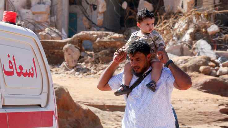 A man holds a boy high on his shoulder while walking through Derna, Libya after the flooding.