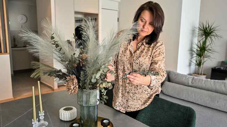 Alisa adjusts a flower centerpiece on the table of an apartment.