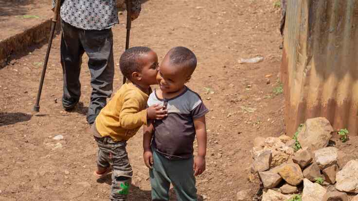 Two young children in Ethiopia embrace outside. They smile together.