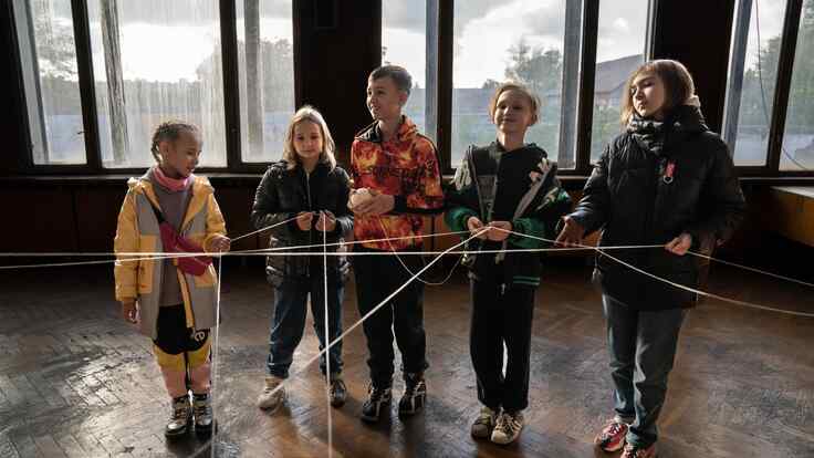 A group of children hold pieces of string while standing in a row to complete a group learning activity.