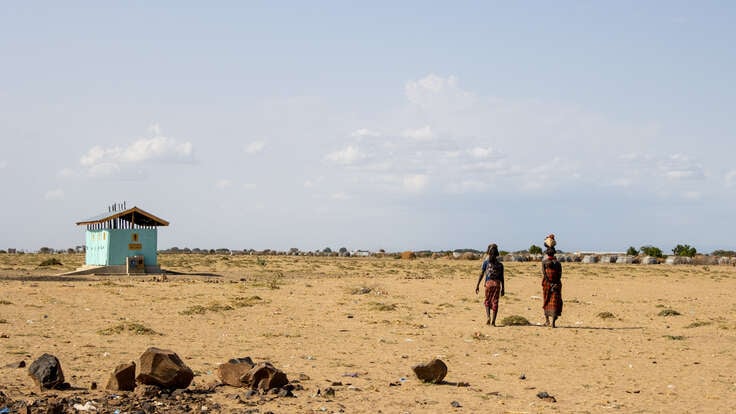Two women walk away from the camera. In the background lies a barren Ethiopia landscape, dotted by an IRC-supported water facility.