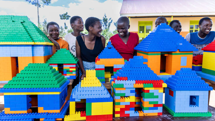 Students stand beside an entire village they made using LEGO bricks, containing houses, schools, churches and mosques.