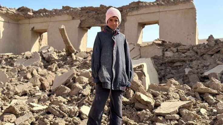 En pojke står framför ett raserat hus efter en jordbävning i Afghanistan.