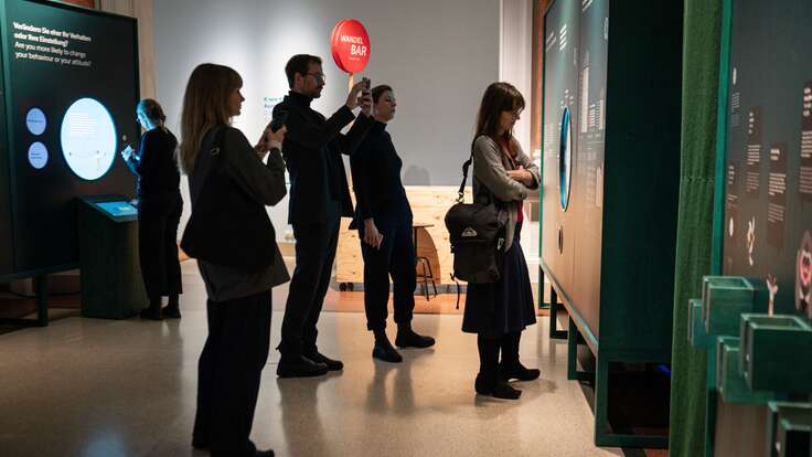 Eine Gruppe von Menschen, die in einem Raum stehen und sich Bidler einer Ausstellung anschauen