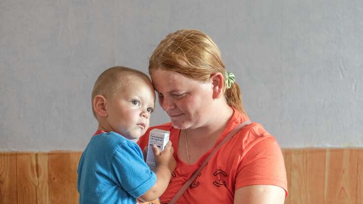 A mother holds her young son in her arms, looking down and smiling at him.