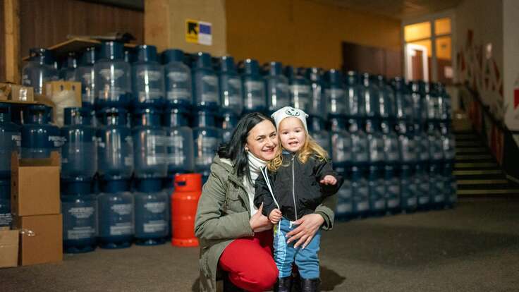 A Ukrainian mother with her young child in front of bottles of water provided by EU funding