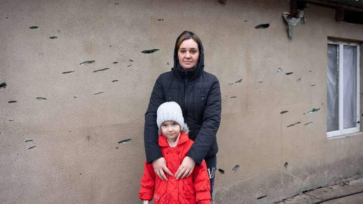 Oleksandra und ihre Mutter Liudmyla stehen vor ihrem beschädigten Zuhause in Cherson, Ukraine. Granatsplitter eines nahegelegenen Raketenangriffs haben das Haus getroffen. IRC unterstützt die Familie mit direkter finanzieller Hilfe.