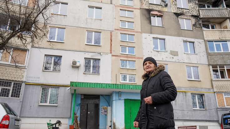 Kateryna stands in front of her apartment in Ukraine, which shows shelling damage 