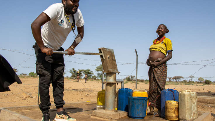 En man pumpar vatten vid en vattenstation i Etiopien, bredvid honom står en gravid kvinna med vattendunkar.