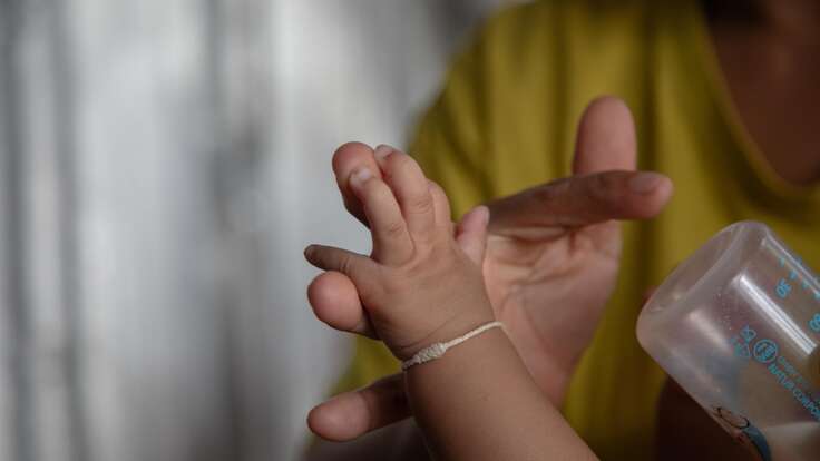 Nwe holds a baby bottle and her baby's hand.