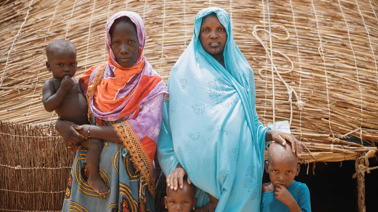 Två mammor står framför ett hus med sina barn.