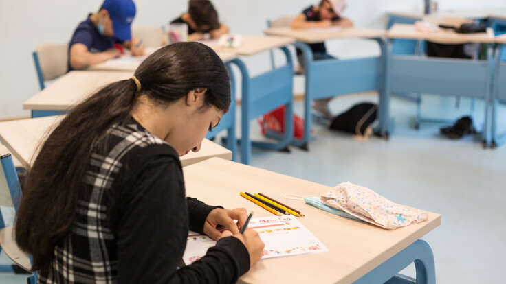 En flicka sitter vid en skolbänk och skriver. 